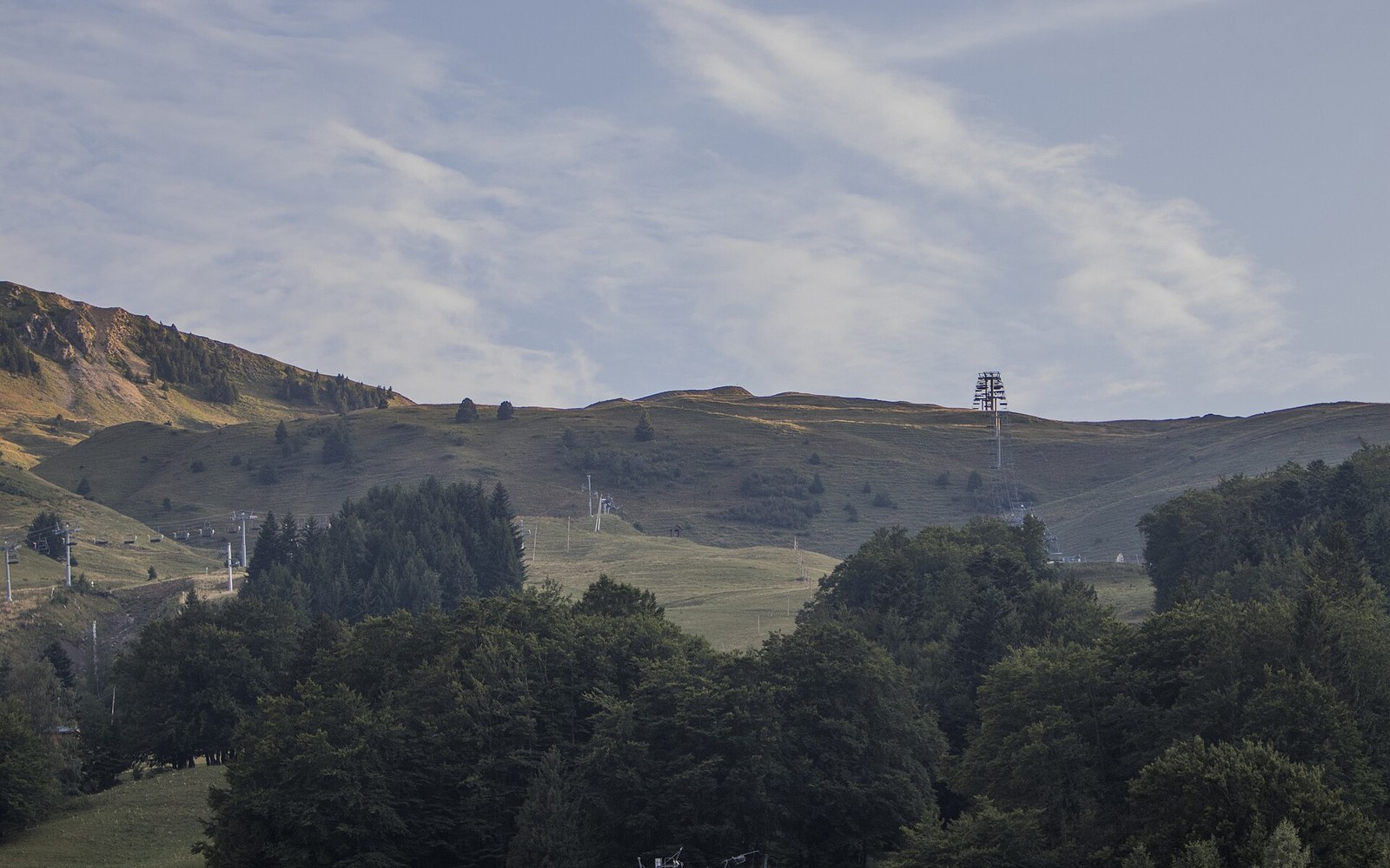 Rolling green hillsides with ski lift pylons rising above a forested slope