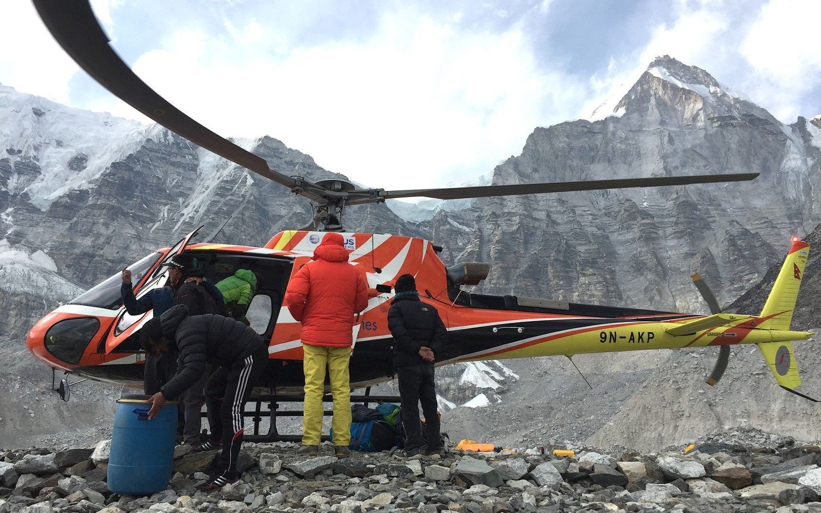 Rescue helicopter grounded on rocky terrain surrounded by snow-capped mountain peaks