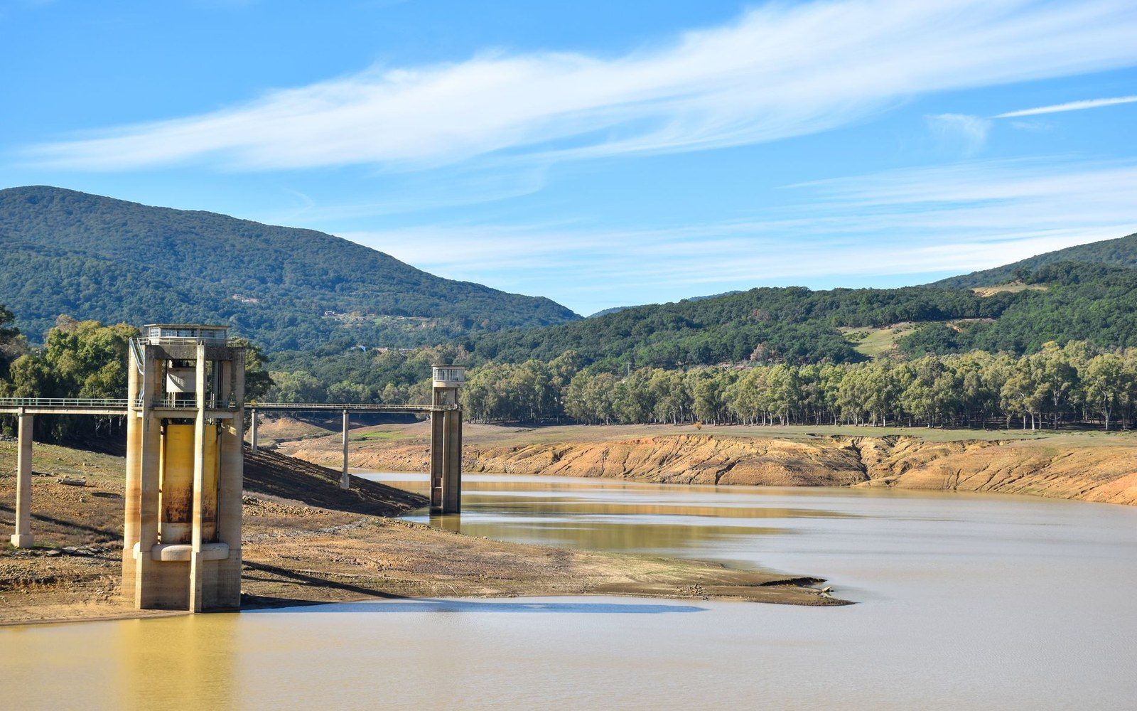 Concrete water intake towers stand in a reservoir with exposed dry banks and hills beyond